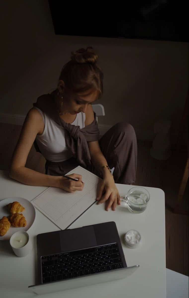 Einefrau, Die An Einem Tisch Auf Einem Laptop Schreibt.