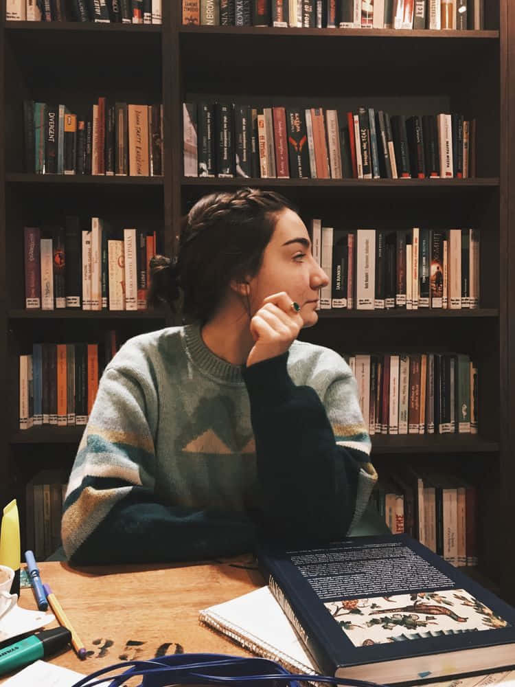 A Girl Sitting At A Table In Front Of Bookshelves