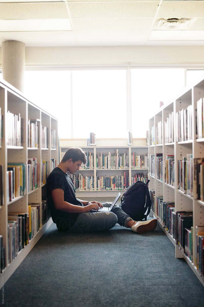 A Man Sitting On The Floor In A Library