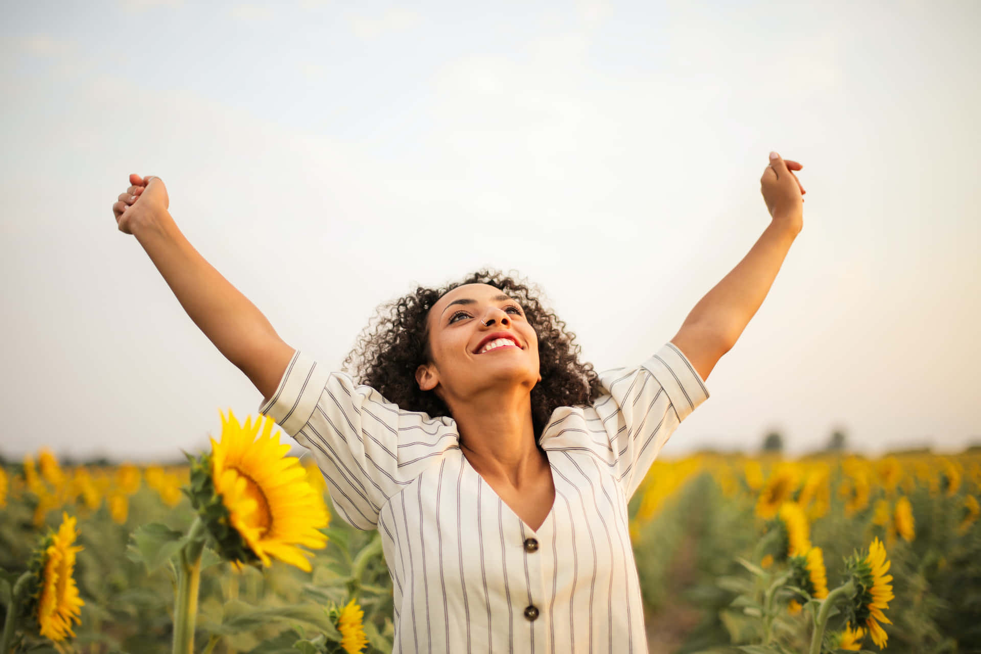 Woman Standing In Sunflower Field With Arms Raised