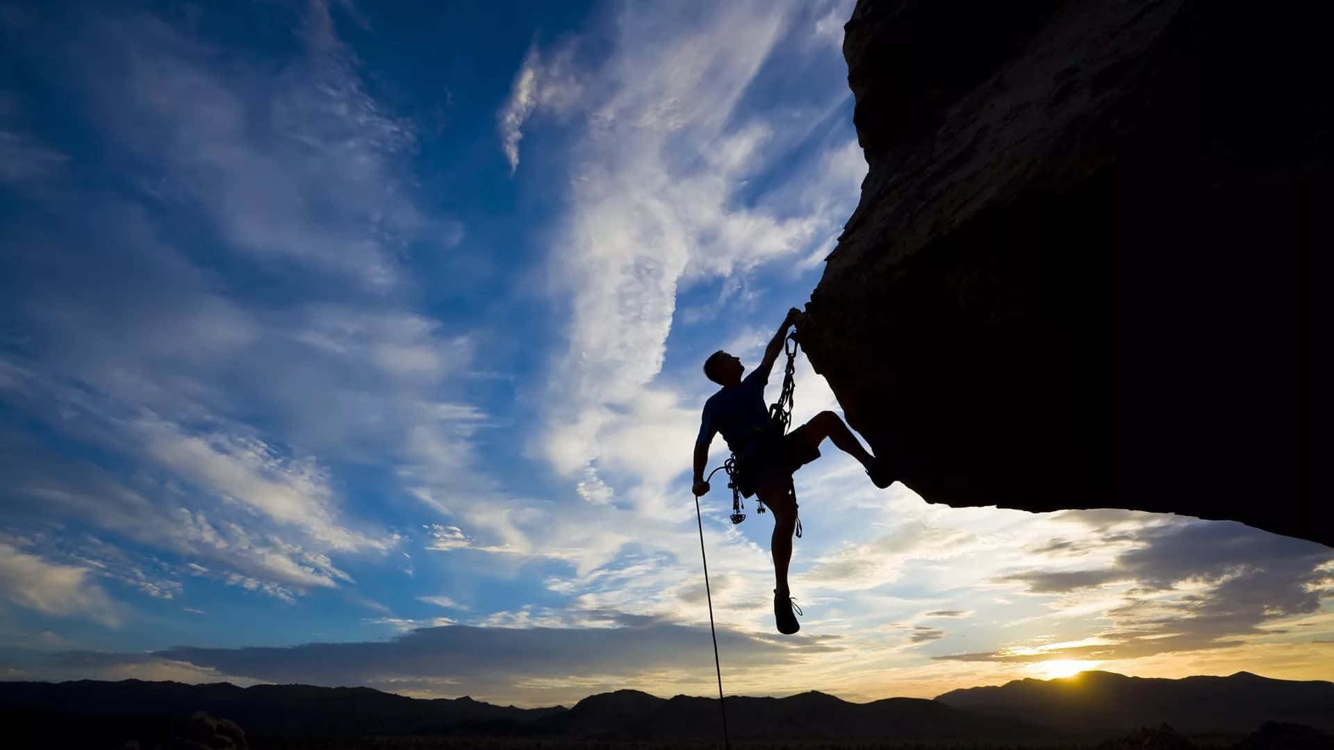 A Man Is Climbing A Rock At Sunset