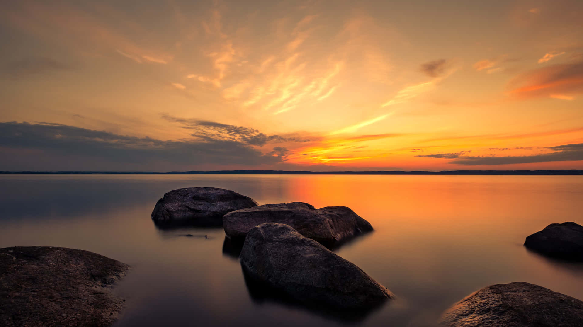 A Sunset With Rocks And Water In The Background