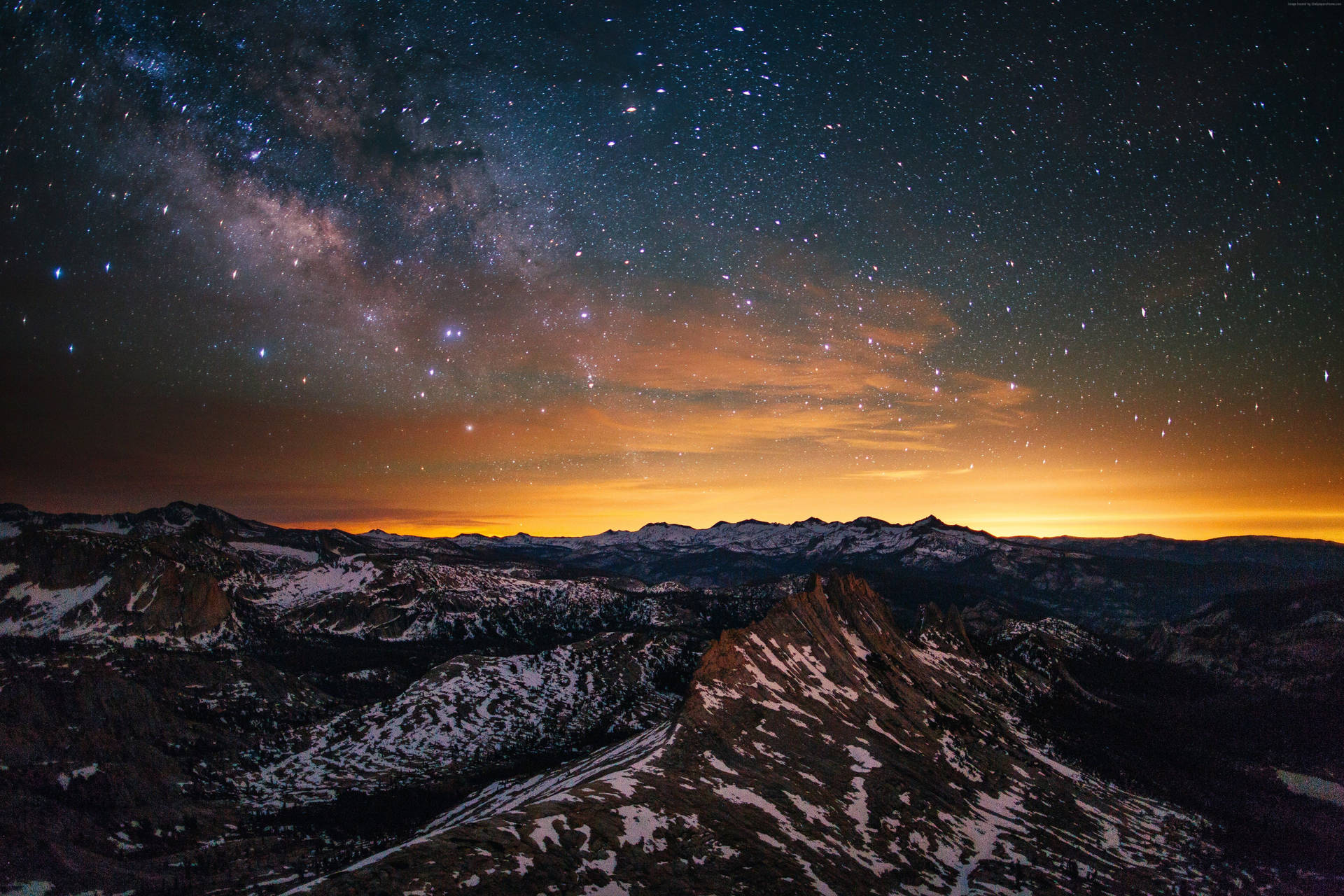 A blanket of stars above a peaceful orange and pink horizon Wallpaper