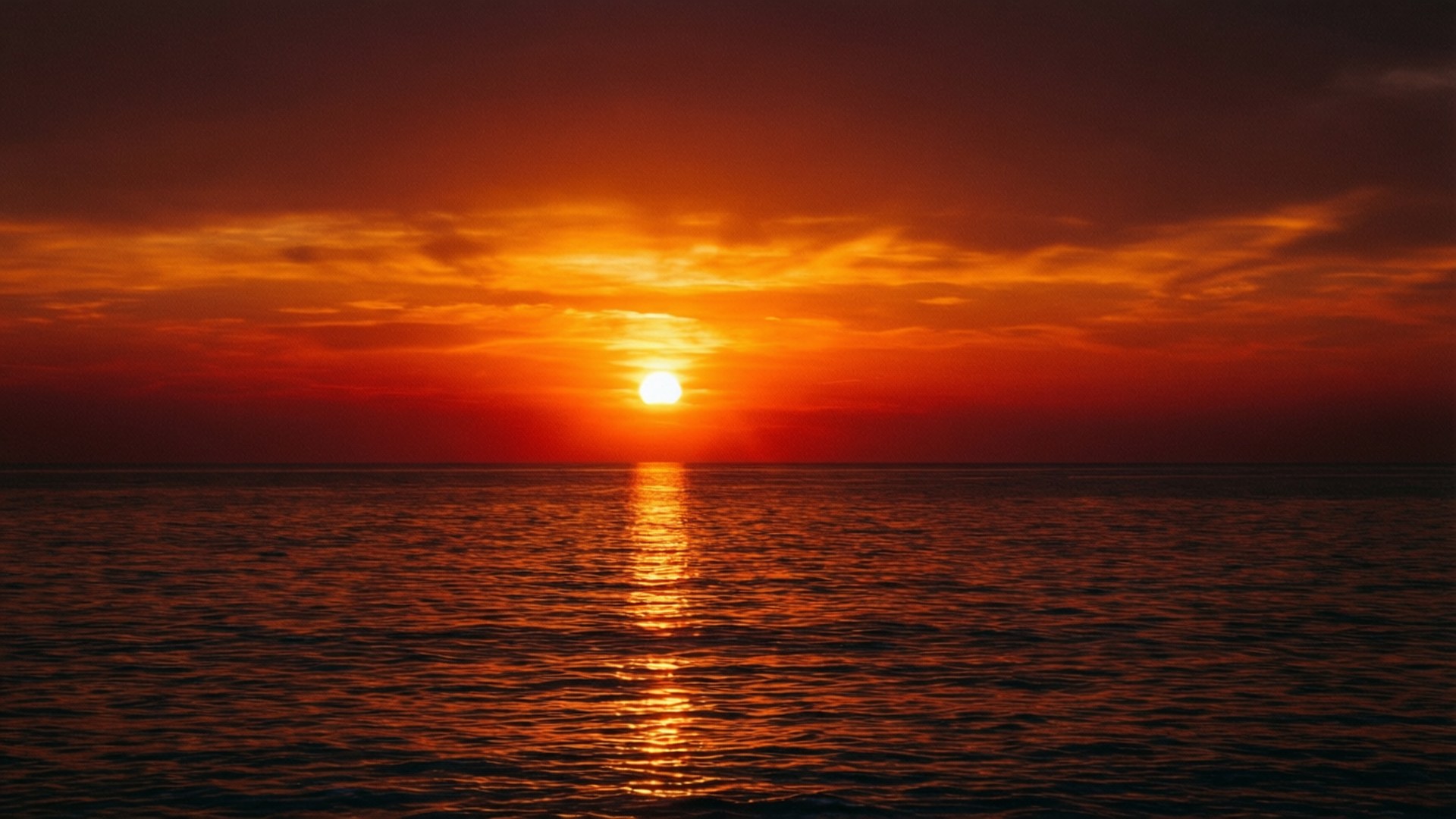 Ein symmetrischer Sonnenuntergang über dem Meer mit orangefarbenen und roten Reflexionen.