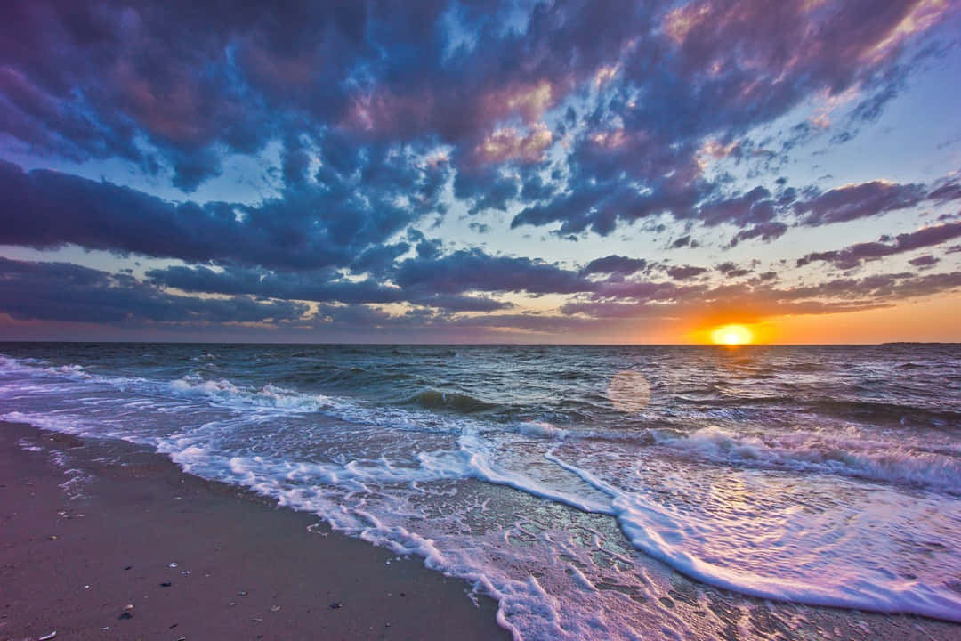 Enjoy the breathtaking beauty of a golden sun setting behind the waves Wallpaper