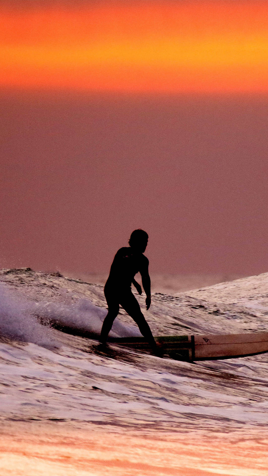 Surfingunder En Orange Solnedgångshimmel. Wallpaper