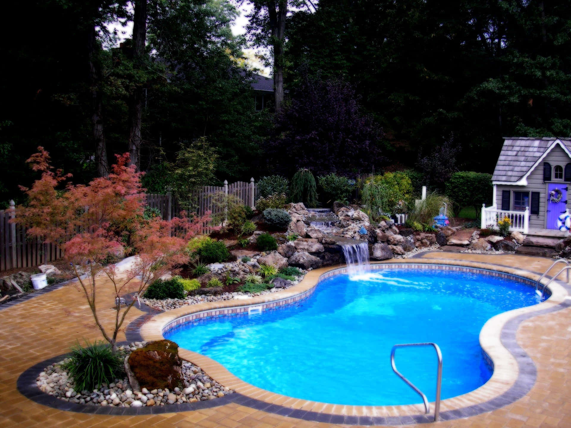 A Swimming Pool With A Waterfall And Landscaping