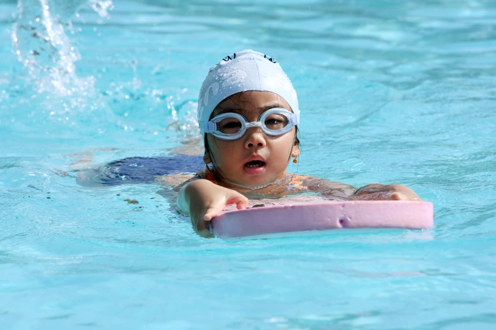 A Young Girl In Goggles Swimming In A Pool