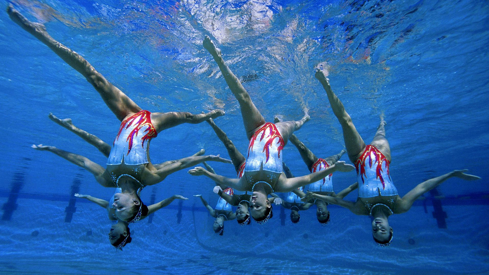 Graceful Underwater Ballet: Synchronized Swimming Upside Down Wallpaper