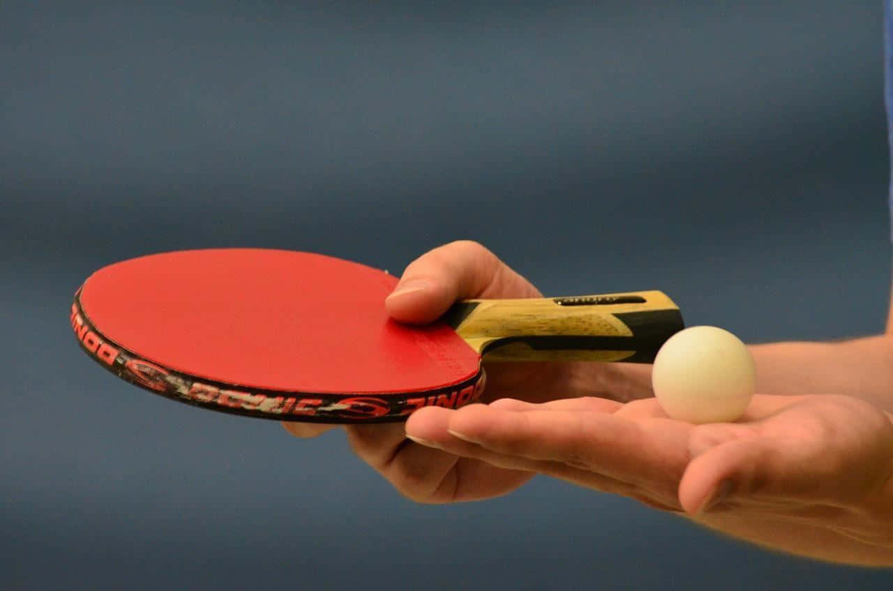 A Person Holding A Ping Pong Paddle And A Ball
