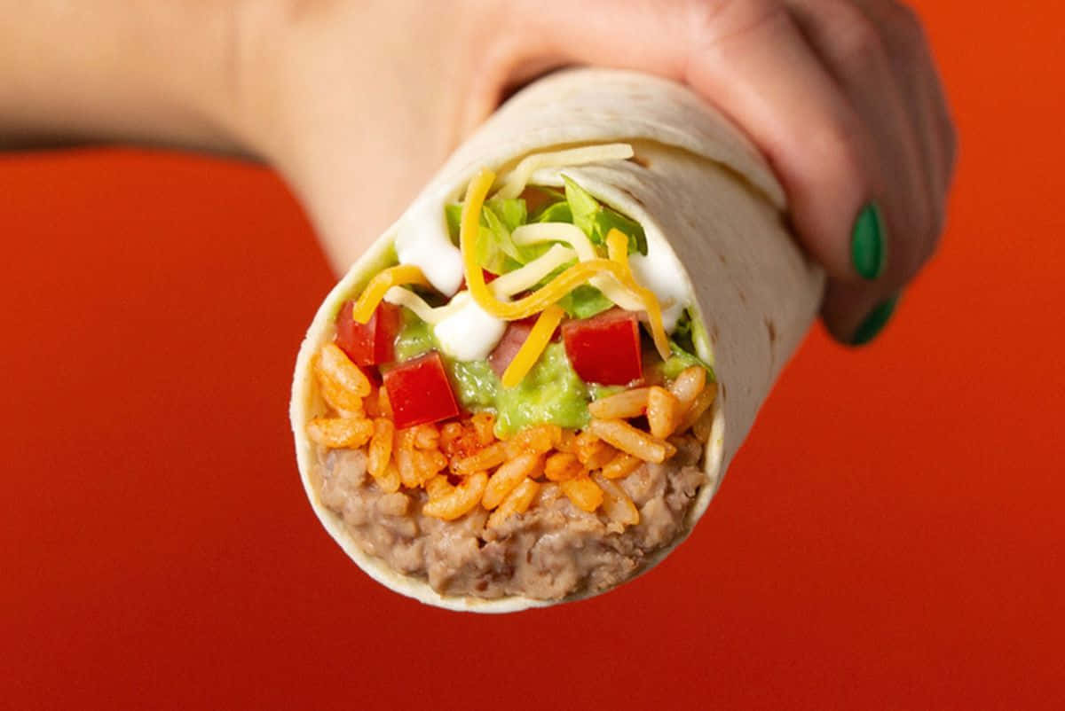 A Person Holding A Burrito With Vegetables And Meat
