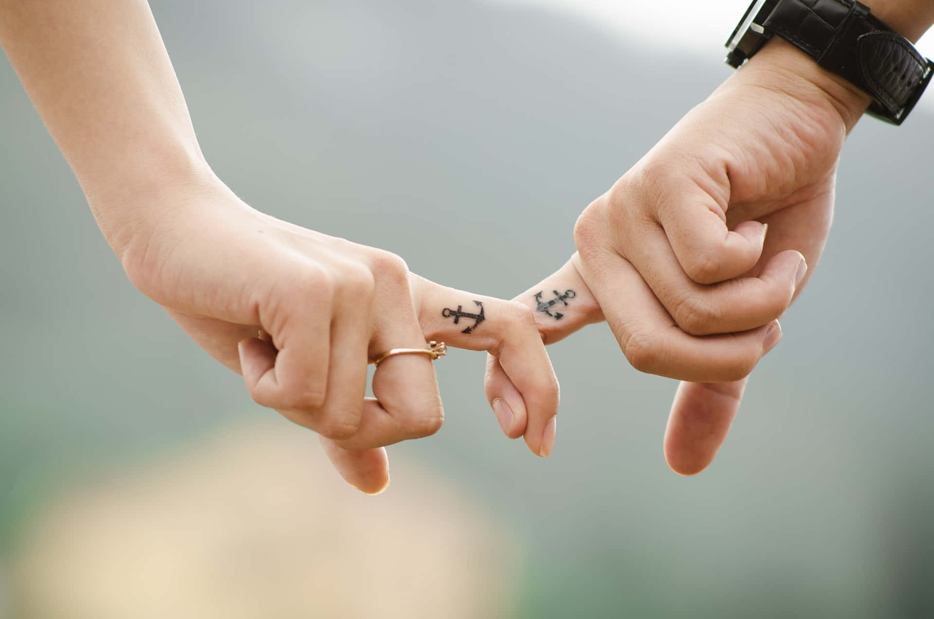 Tangible Holding Of A Couple's Index Fingers With Anchor Tattoos Wallpaper