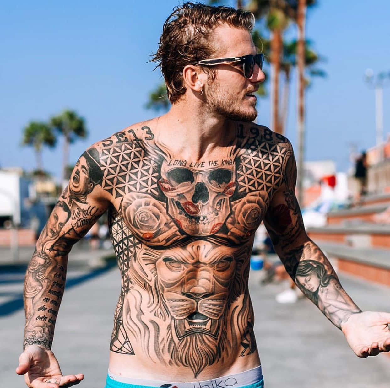 A Man With Tattoos On His Chest Walking Down The Street