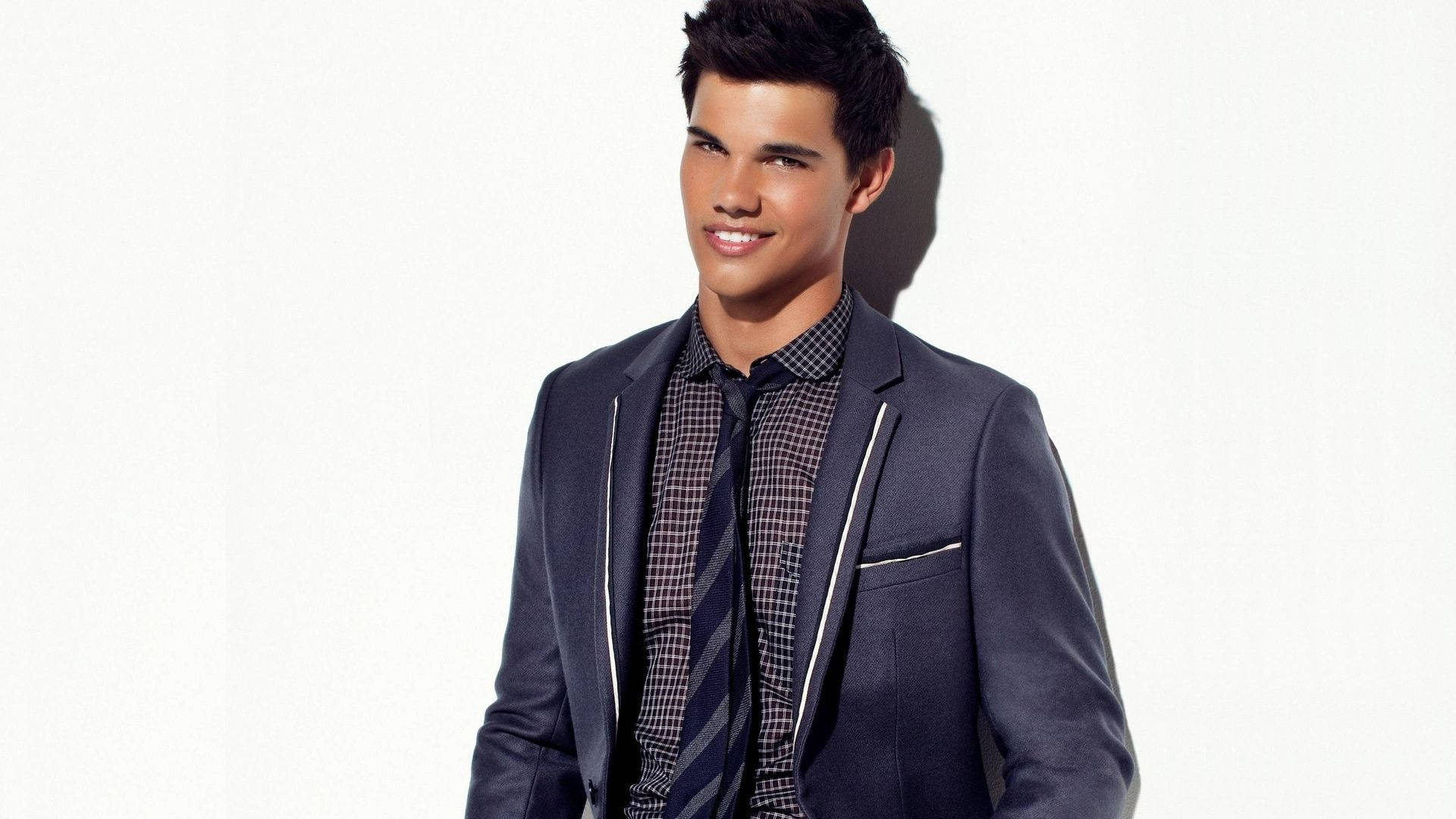 Taylor Lautner i smoking adskiller sig fra den grå baggrund. Wallpaper