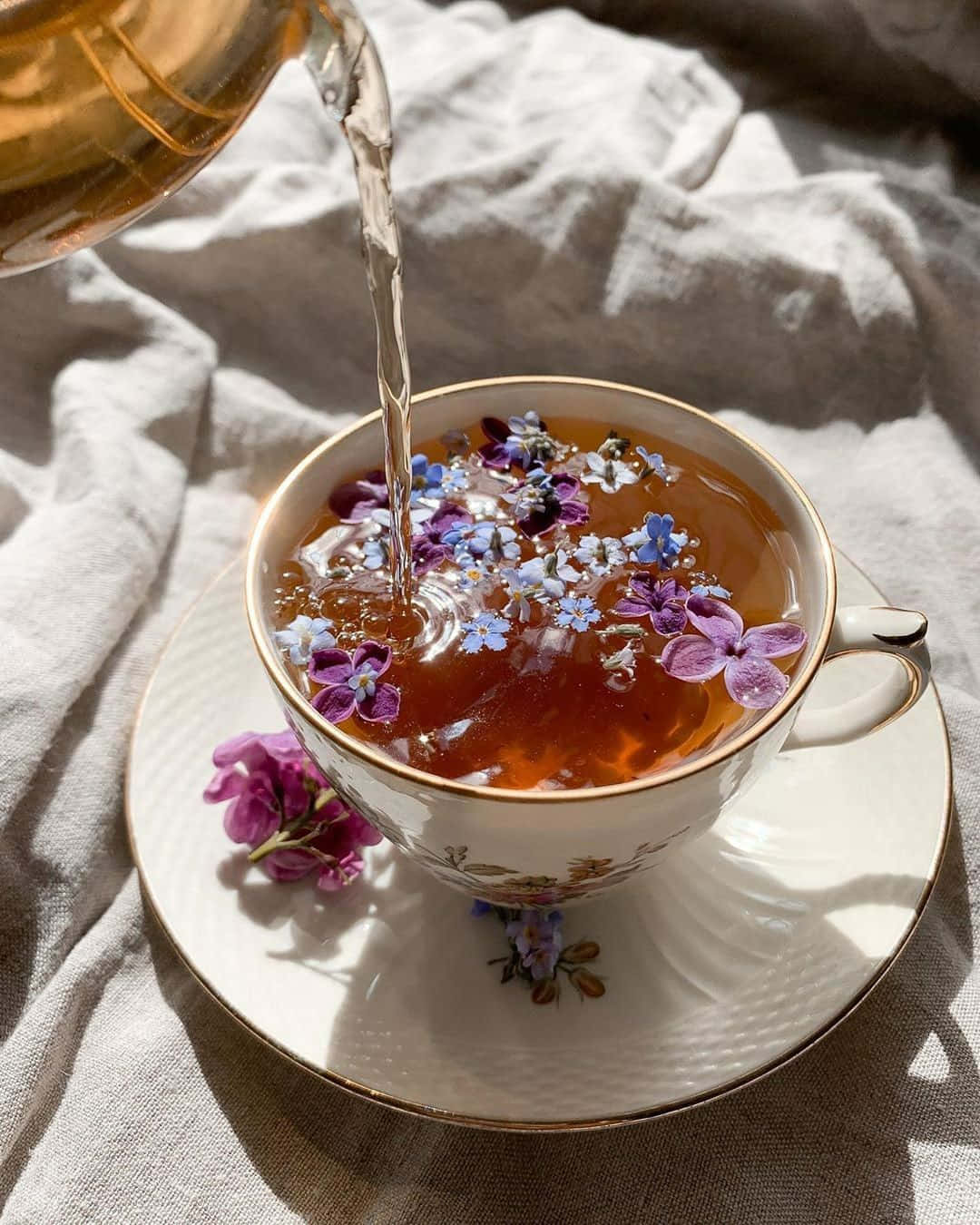 A Cup Of Tea With Flowers Being Poured Into It