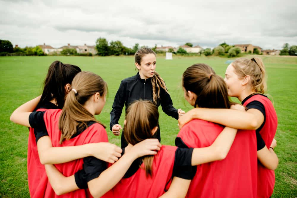 A Group Of Girls Huddled Around A Soccer Coach