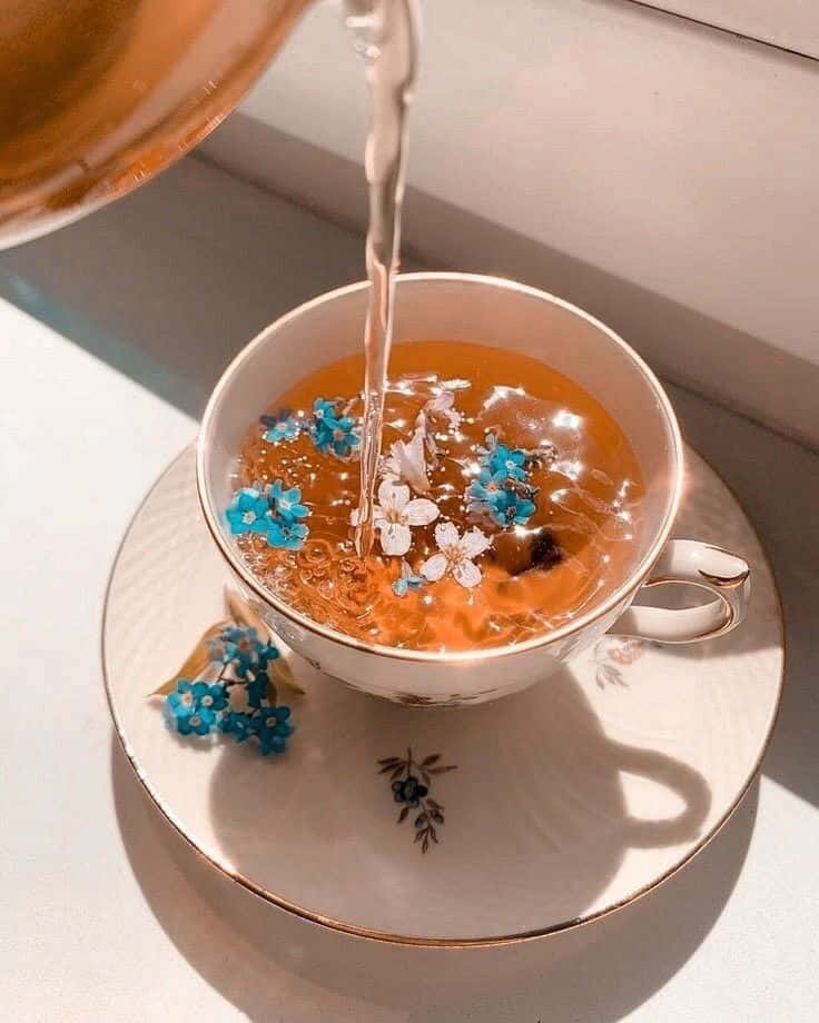 A Cup Of Tea With Blue Flowers Being Poured Into It