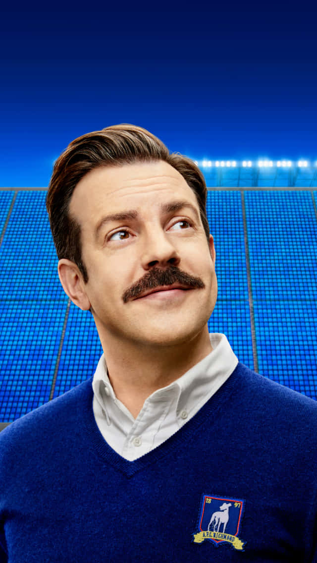 Ted Lasso Character Smiling Against Stadium Backdrop Wallpaper