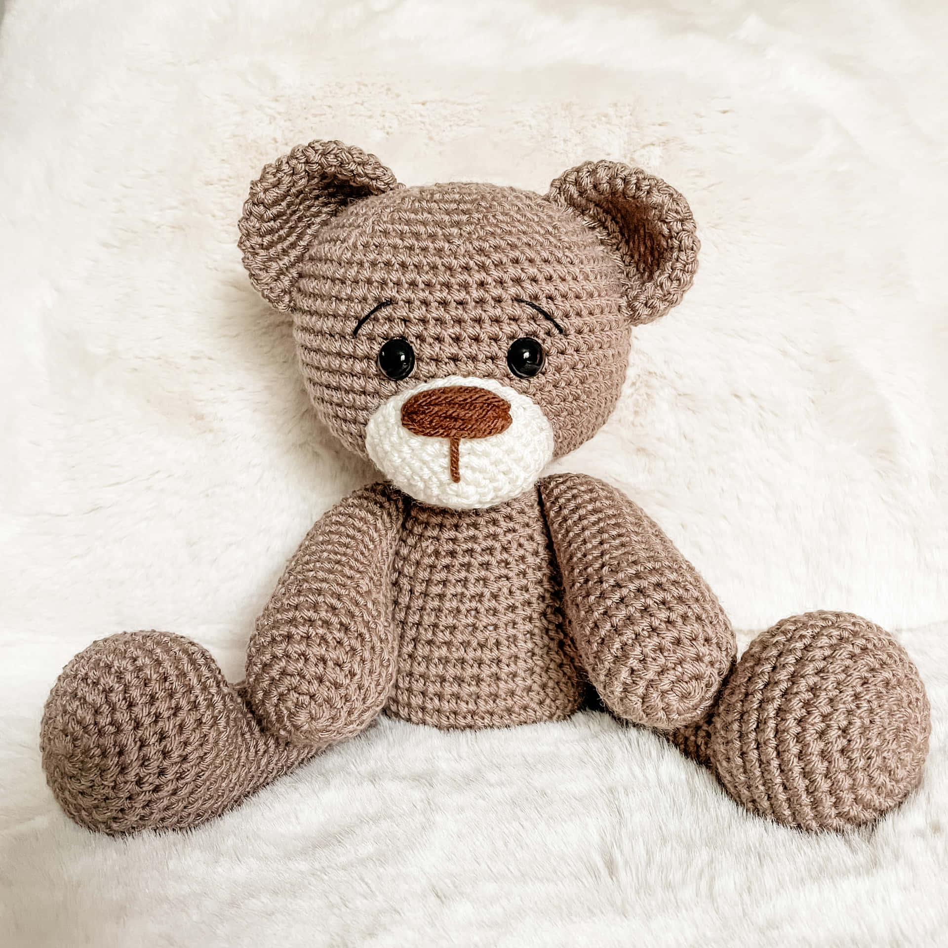 A Crocheted Teddy Bear Sitting On A White Blanket