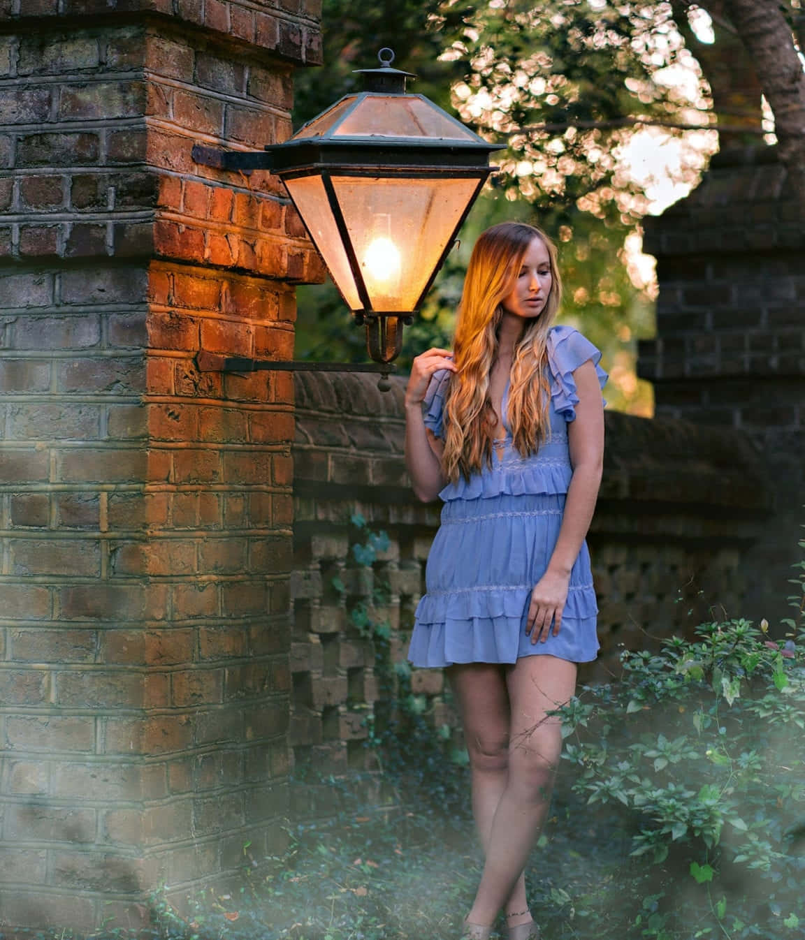 A Woman In A Blue Dress Standing Next To A Brick Wall