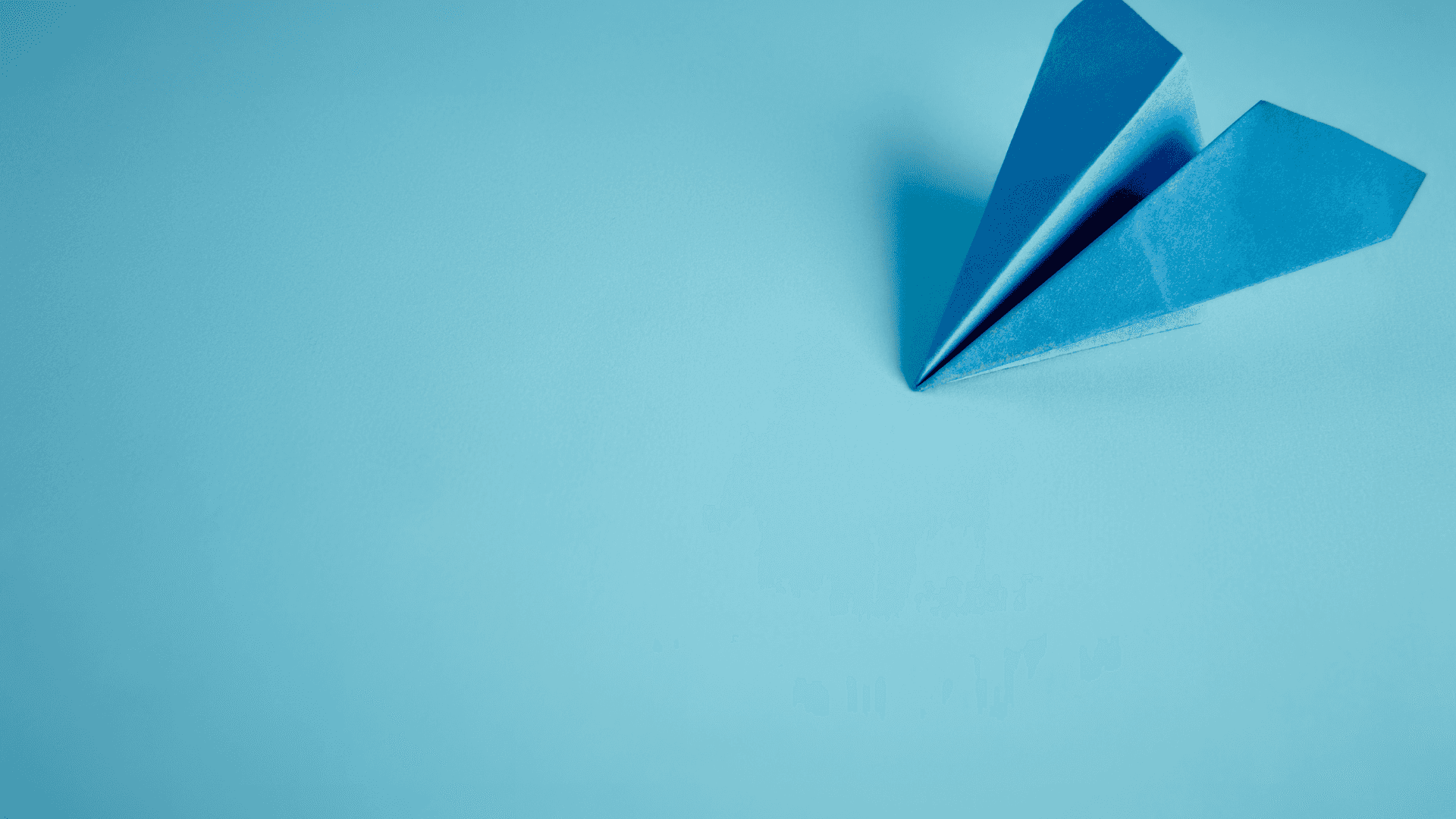 a blue paper airplane on a blue background — A single blue paper airplane rests on a solid blue surface casting a soft shadow.