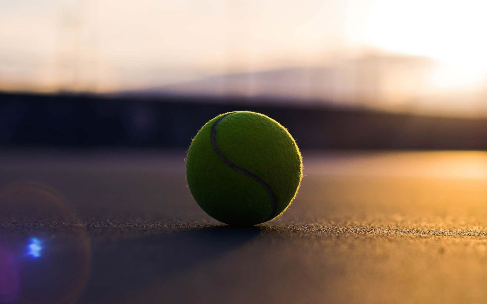 Et frisk tenniskugle liggende på en græsmark klar til spil Wallpaper