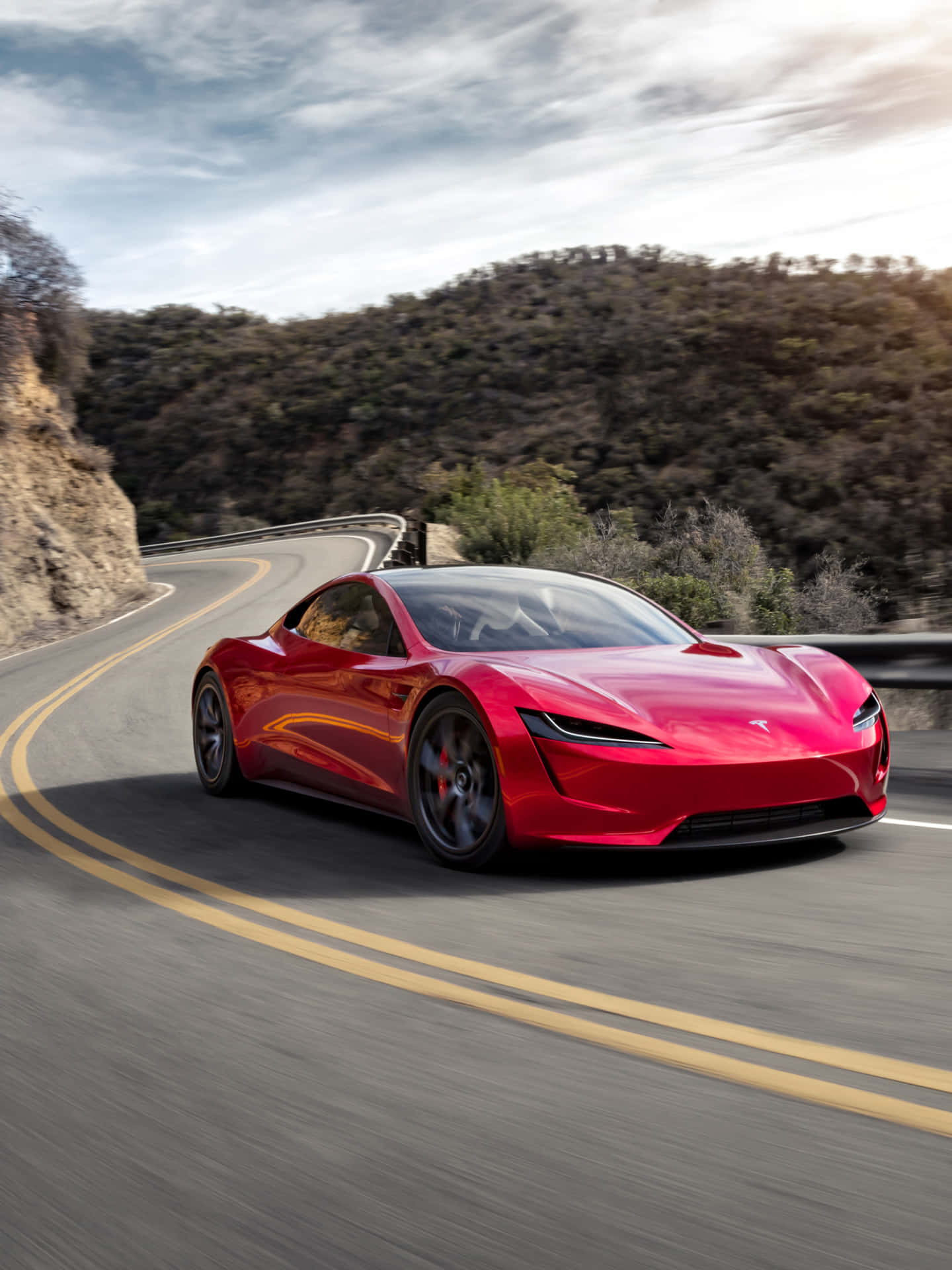 The Red Tesla E-sports Car Is Driving Down A Mountain Road Wallpaper