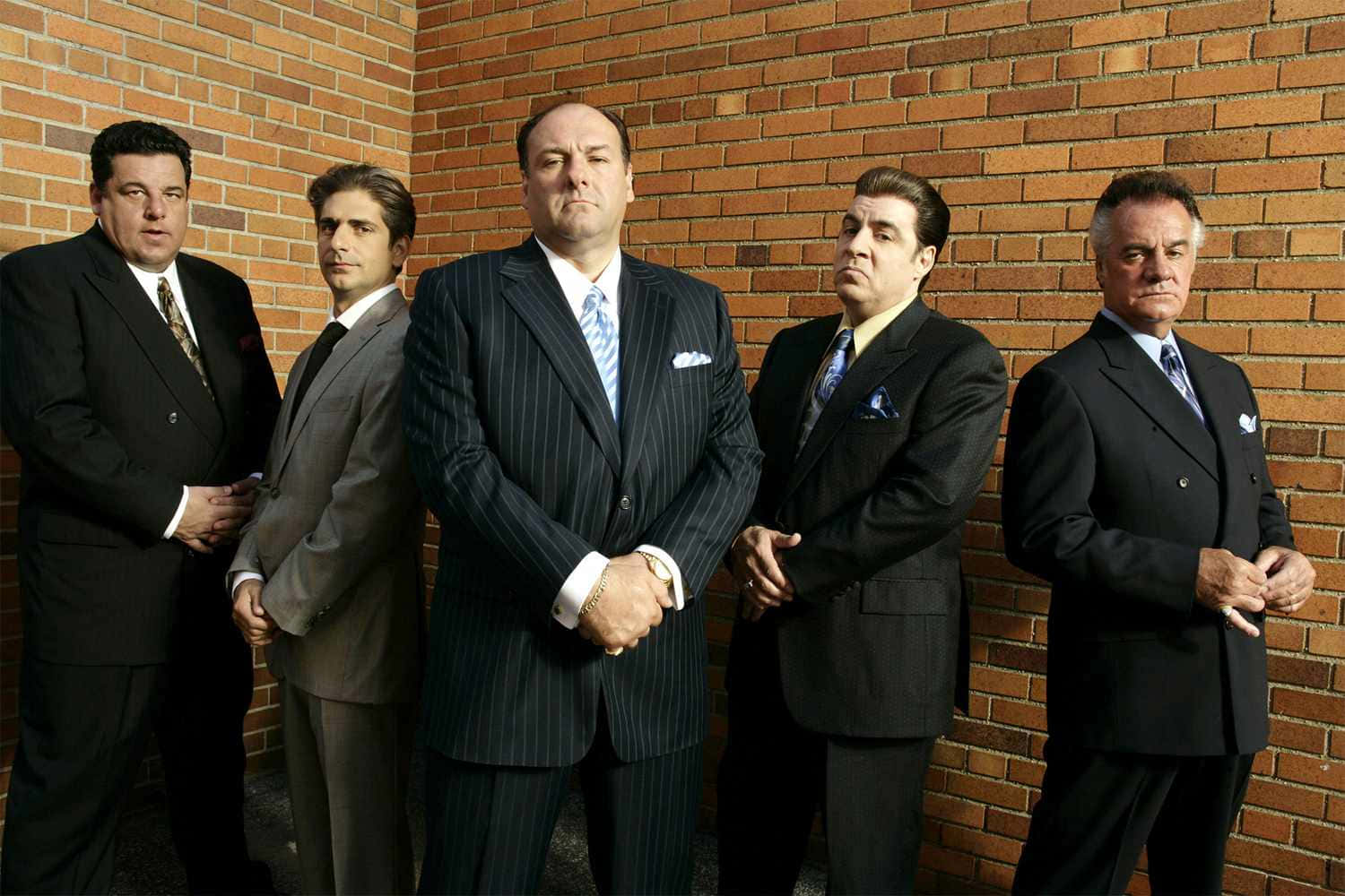 A Group Of Men In Suits Standing Next To A Brick Wall Wallpaper