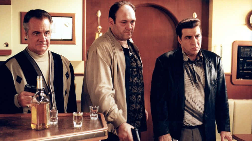 Three Men Standing Next To A Bar With A Bottle Of Liquor Wallpaper