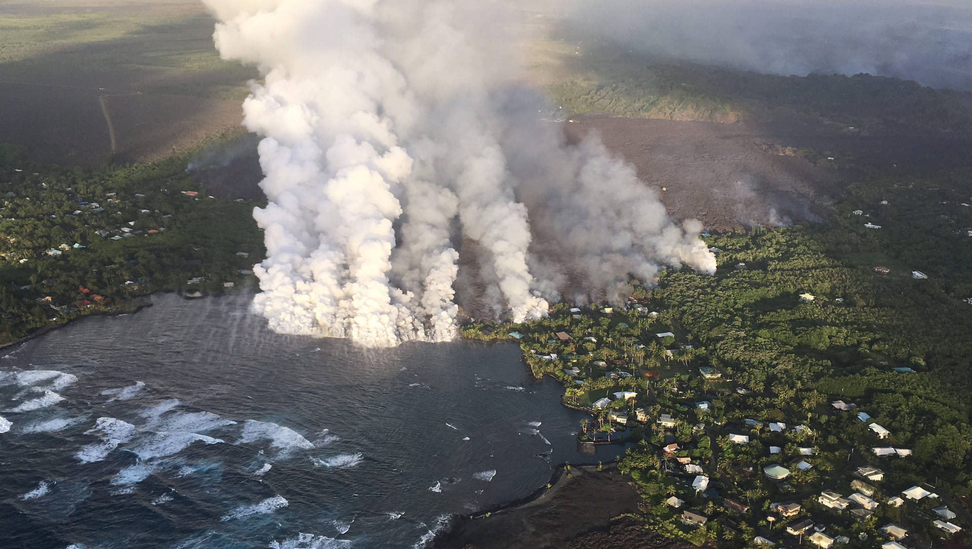 Tykt røg fra Kilauea-vulkanen ruller bag en sandstrand Wallpaper