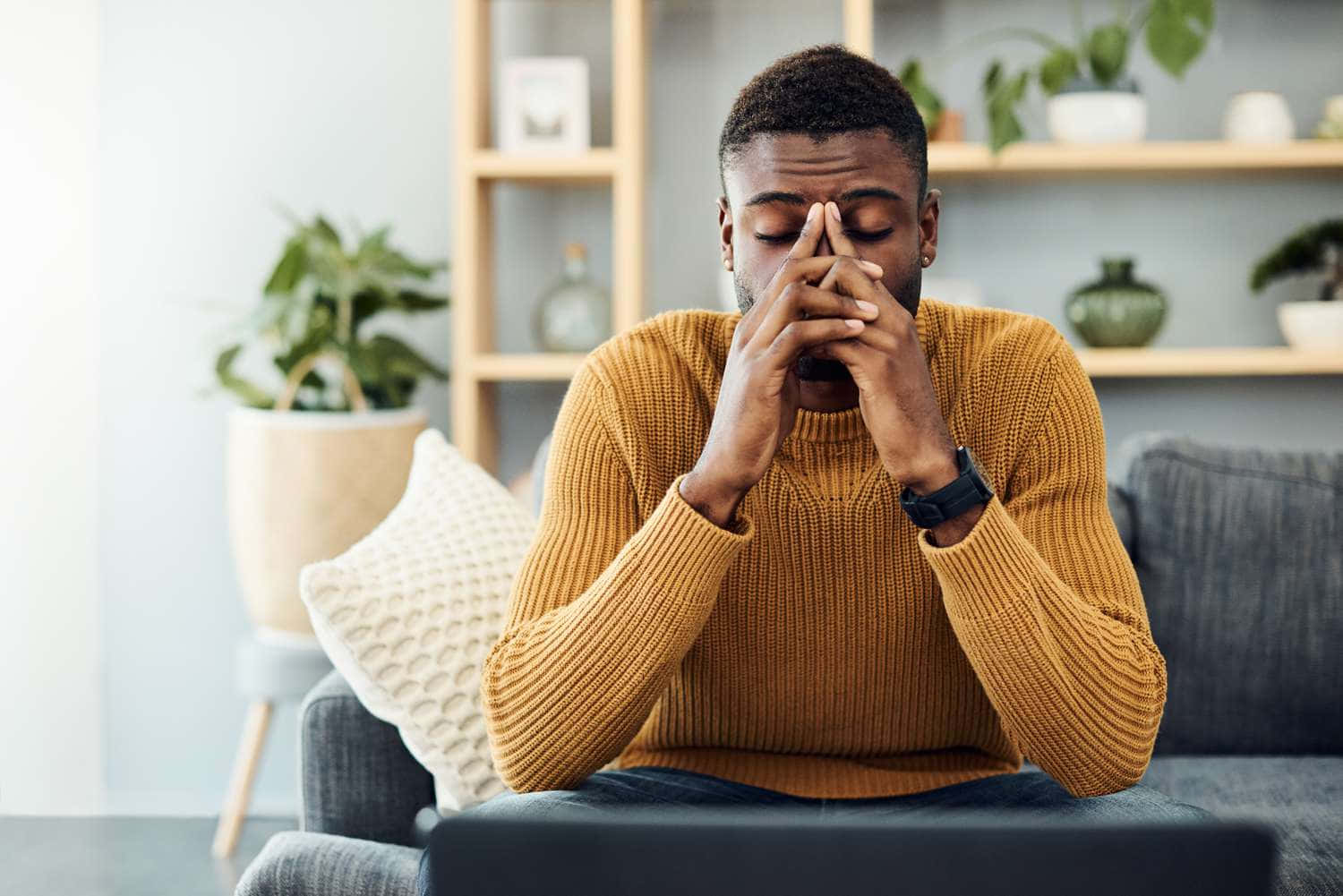 A Man Sitting On A Couch With His Hands On His Face