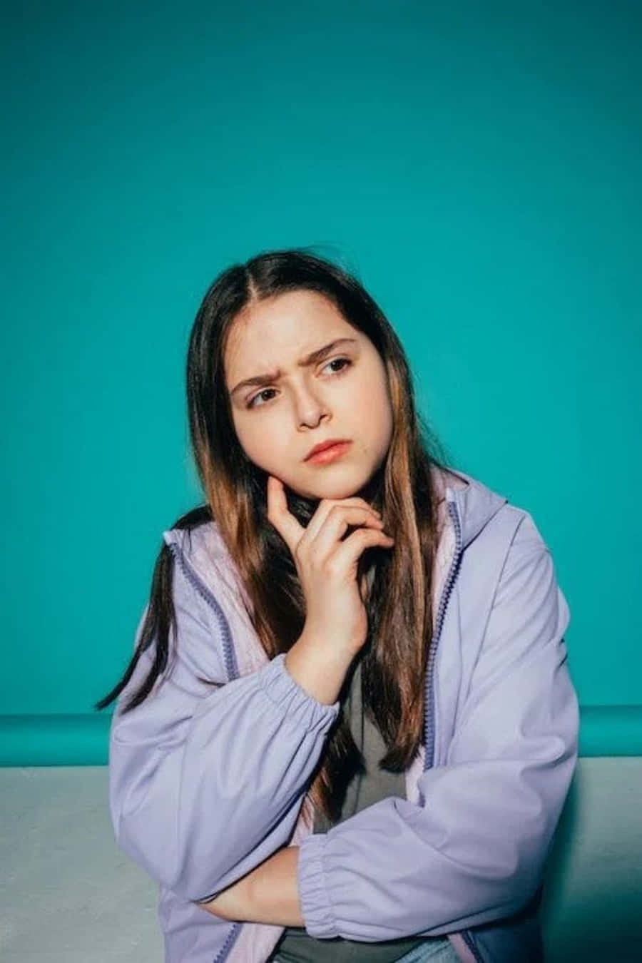 A Young Woman With Long Hair And Blue Jacket Sitting On A Blue Background
