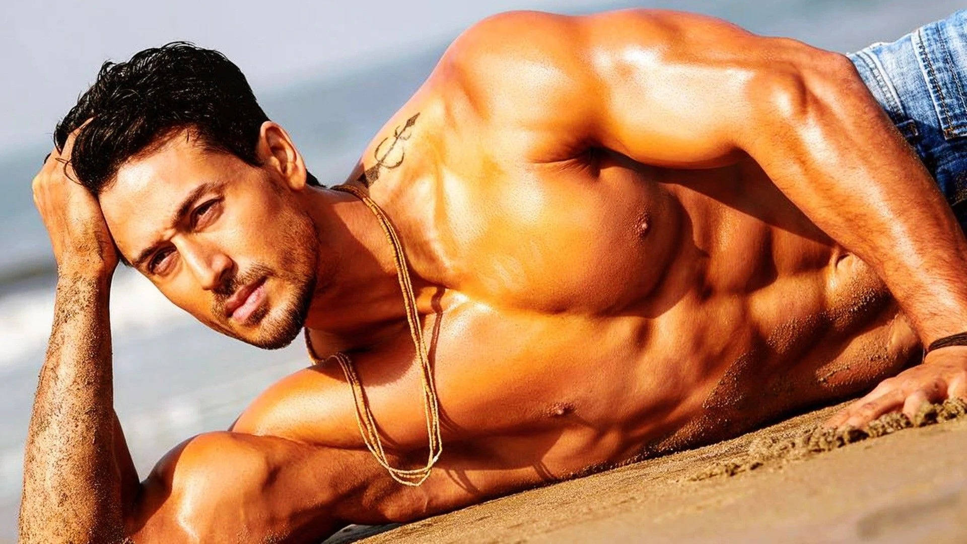 Tiger Shroff Body While Posing On Sand Wallpaper