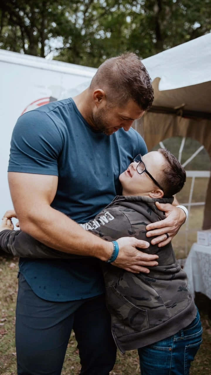 A Man Hugging A Young Boy In Front Of A Tent Wallpaper