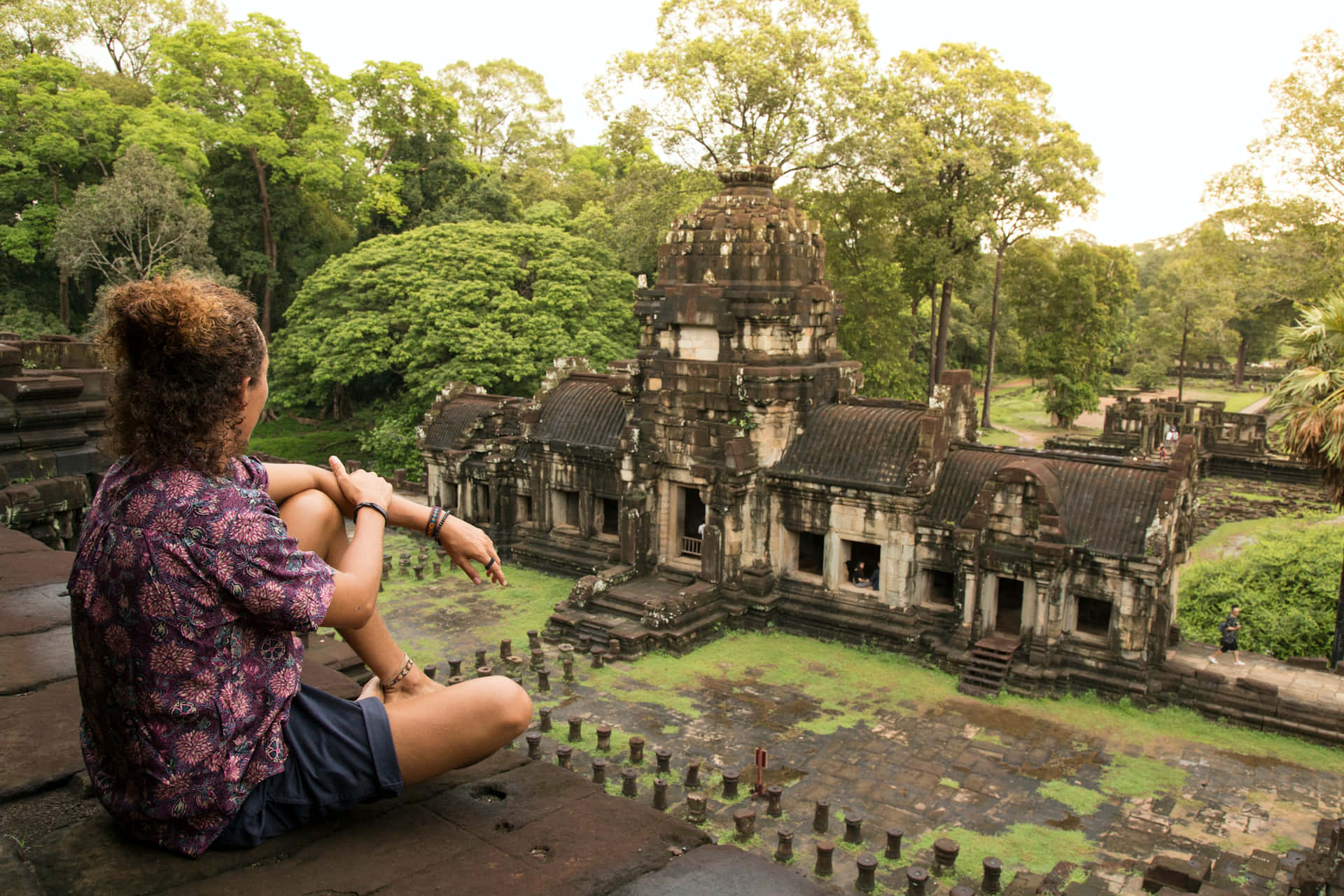Turist siddende på toppen af Angkor Thom-ruiner mod morgensolen Wallpaper