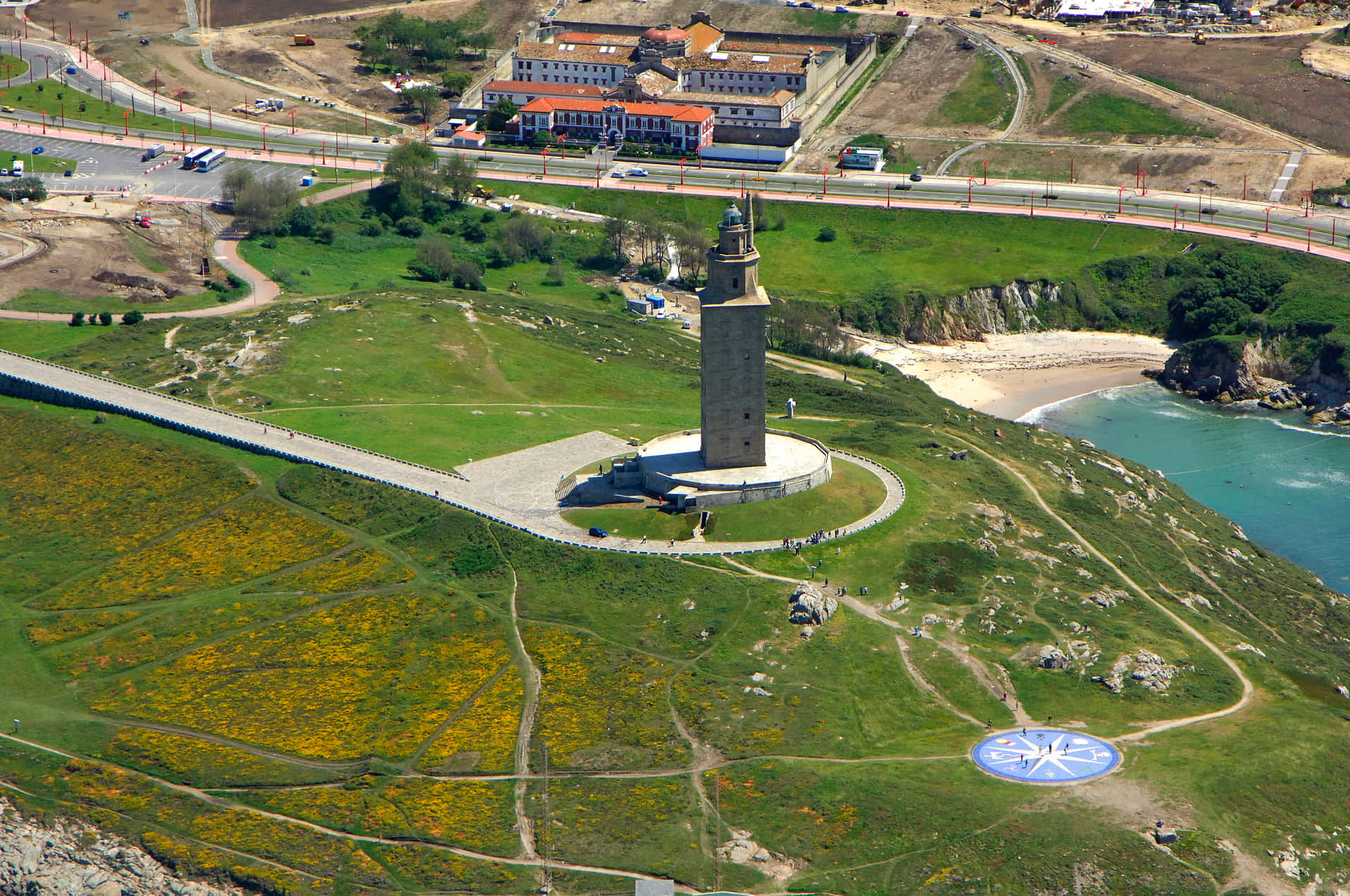 Aerial View of the Majestic Tower of Hercules Surrounded by Lush Green Grass Wallpaper