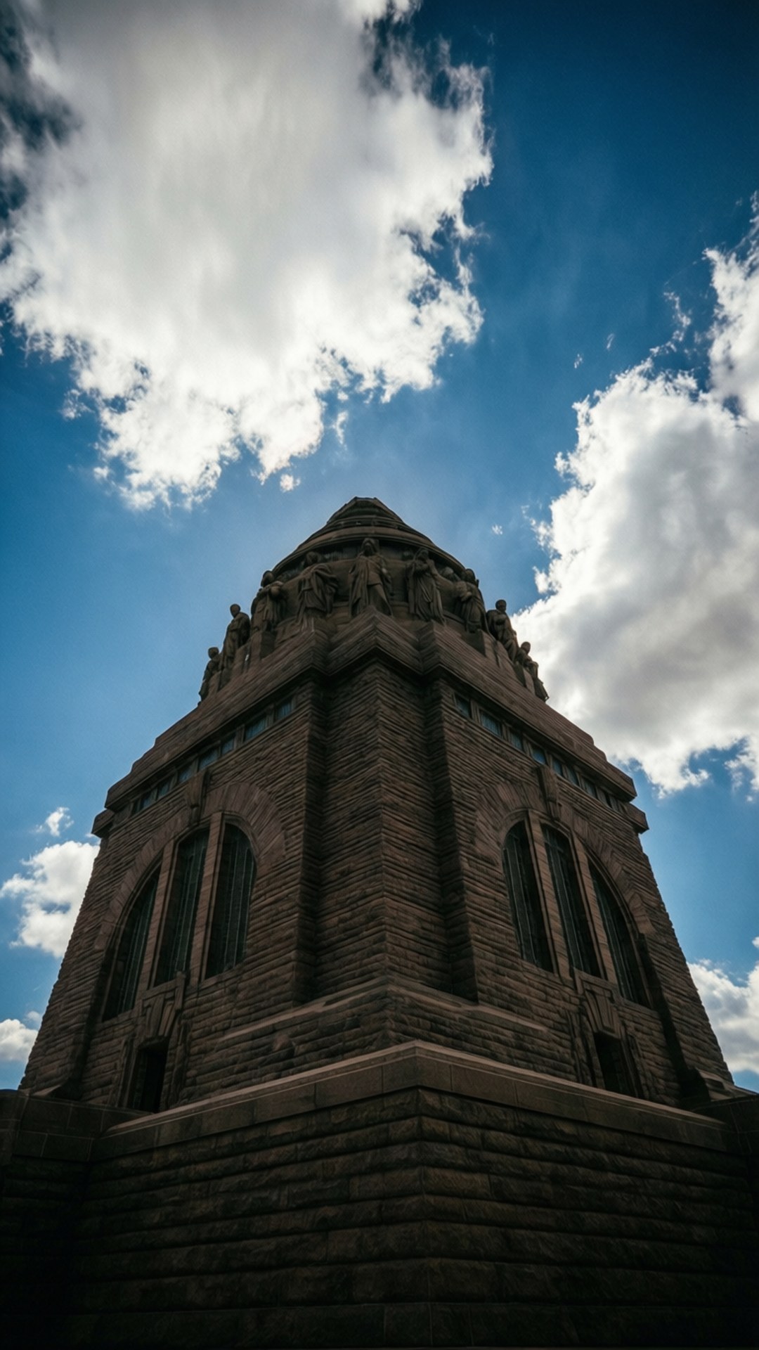Low-angle shot making Voortrekker Monument appear towering against a blue sky with clouds.