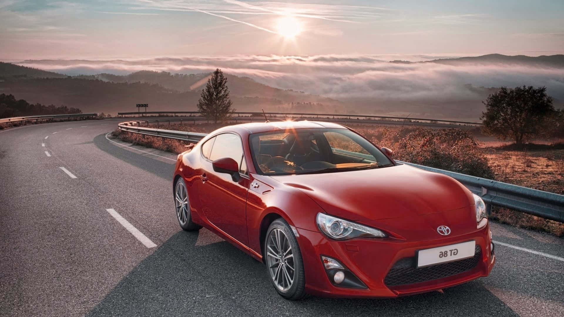 the red toyota 86 is driving down a road Wallpaper