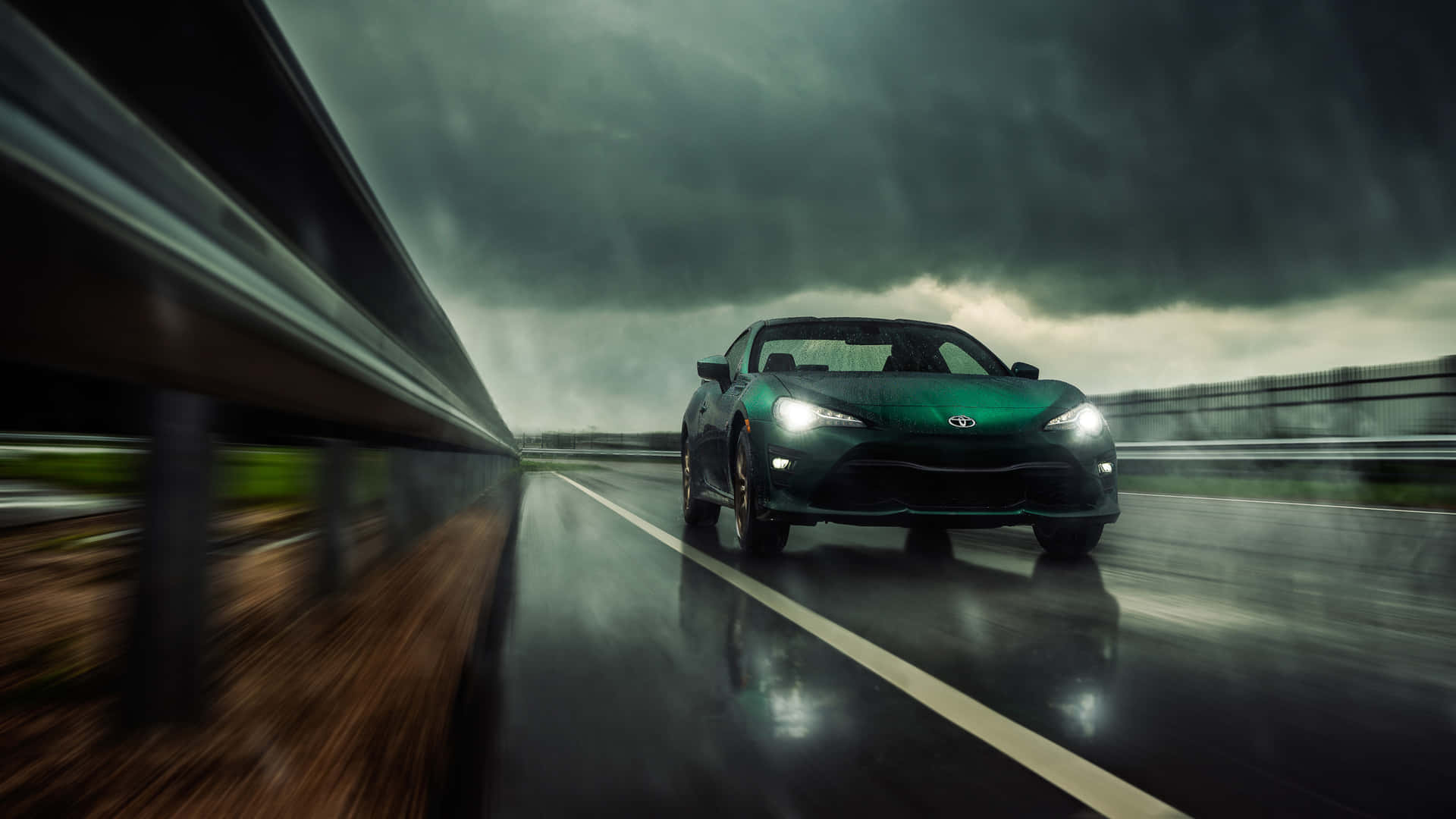 A Green Car Driving On A Rainy Road Wallpaper