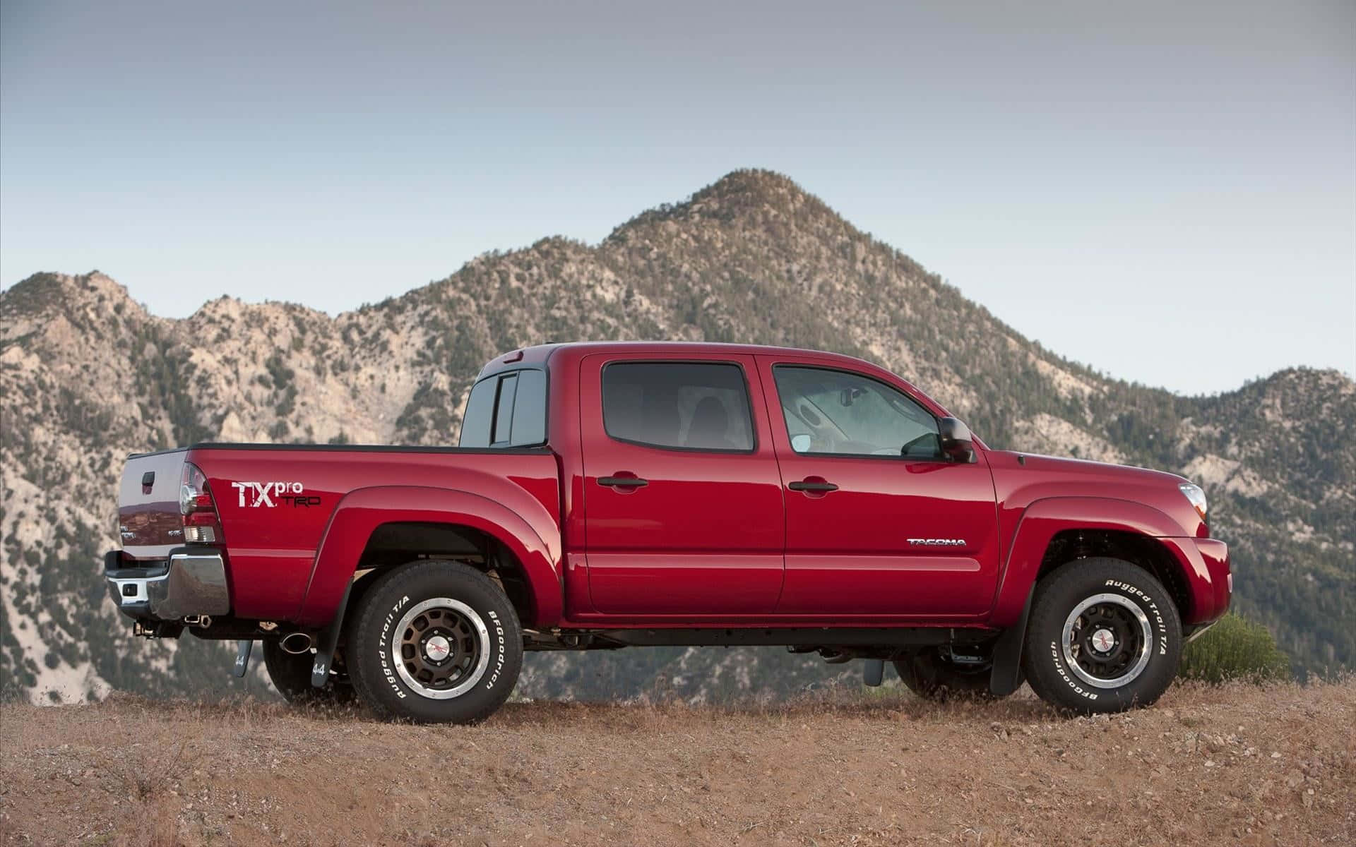 The Red Toyota Tacoma Is Parked In Front Of Mountains Wallpaper