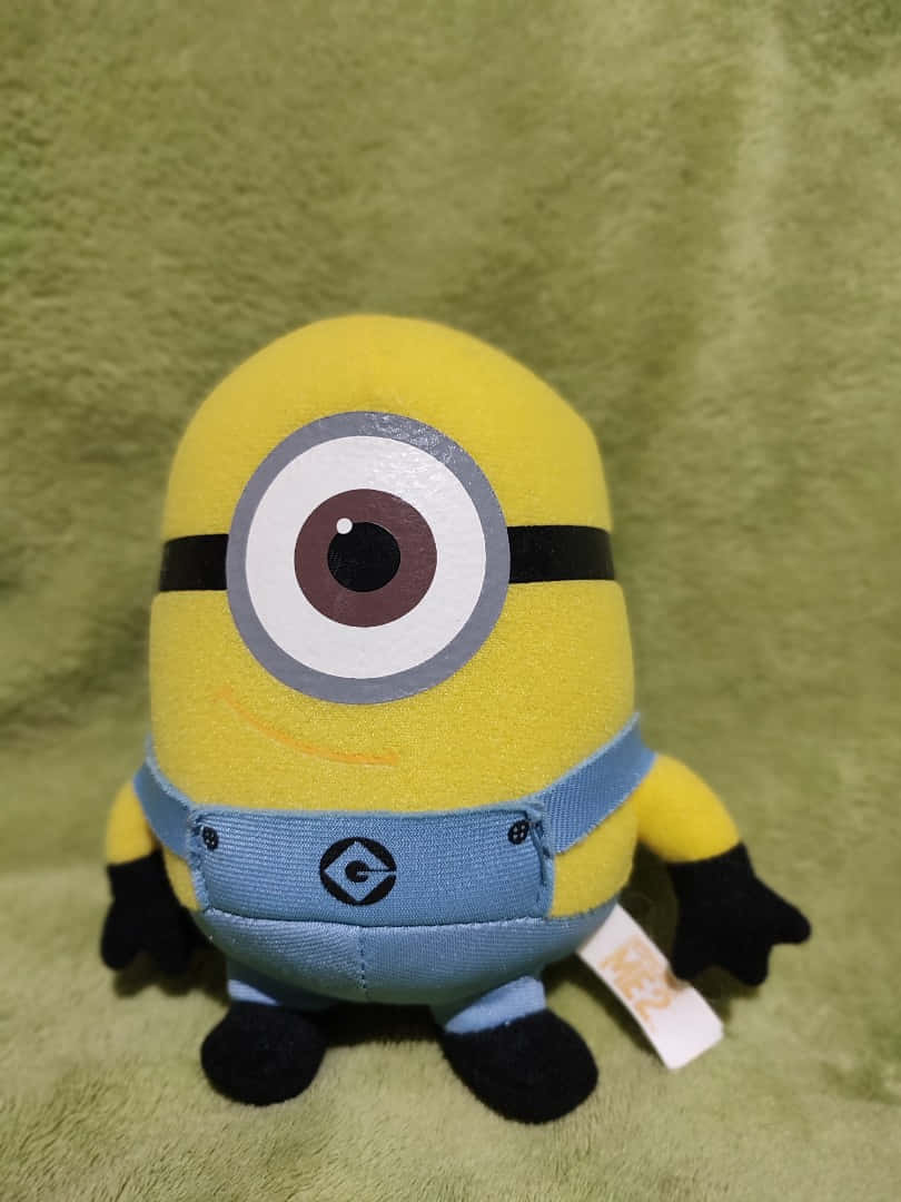 A Minion Stuffed Animal Is Sitting On A Green Background