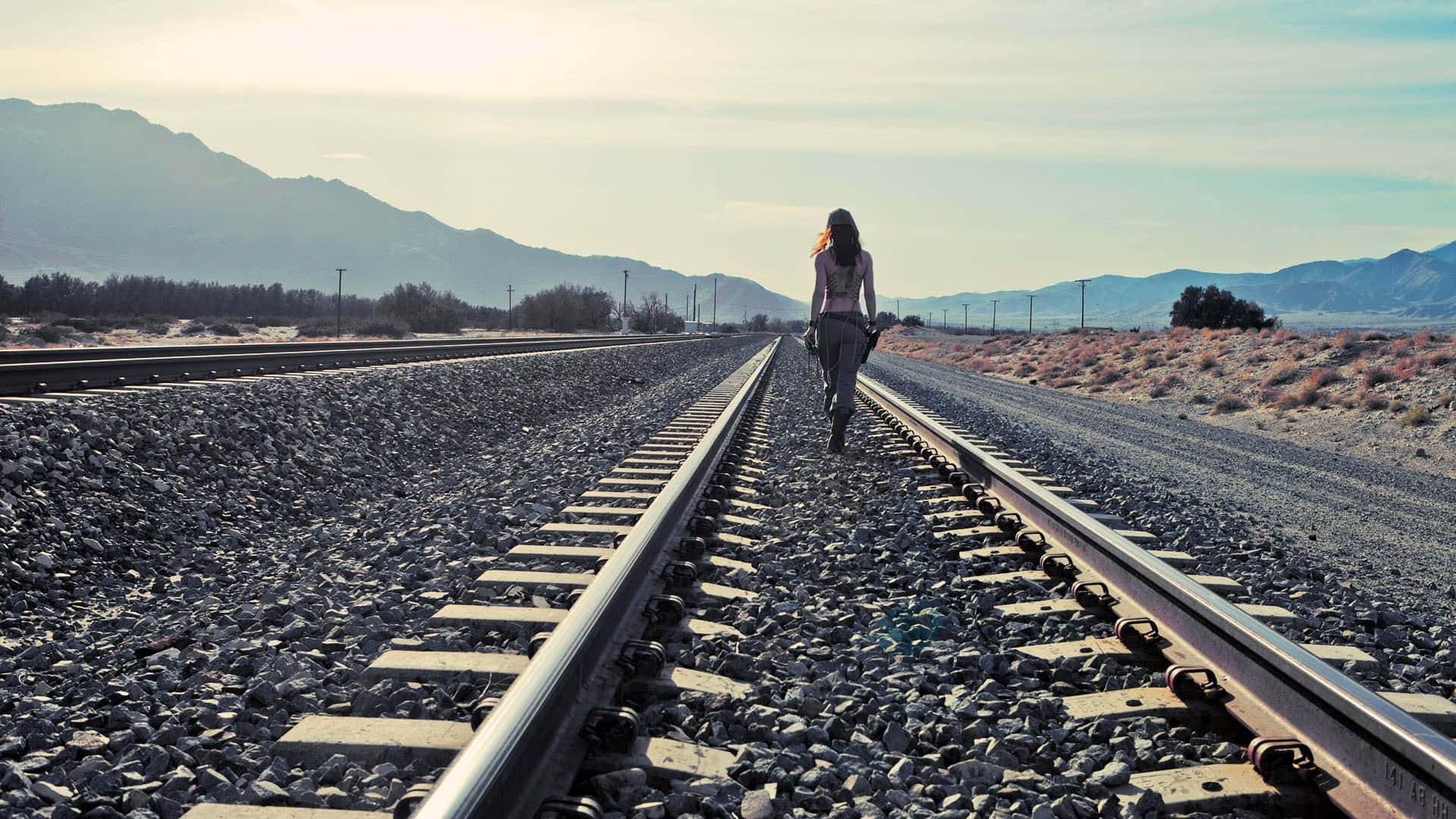 A Woman Walking On Railroad Tracks In The Desert