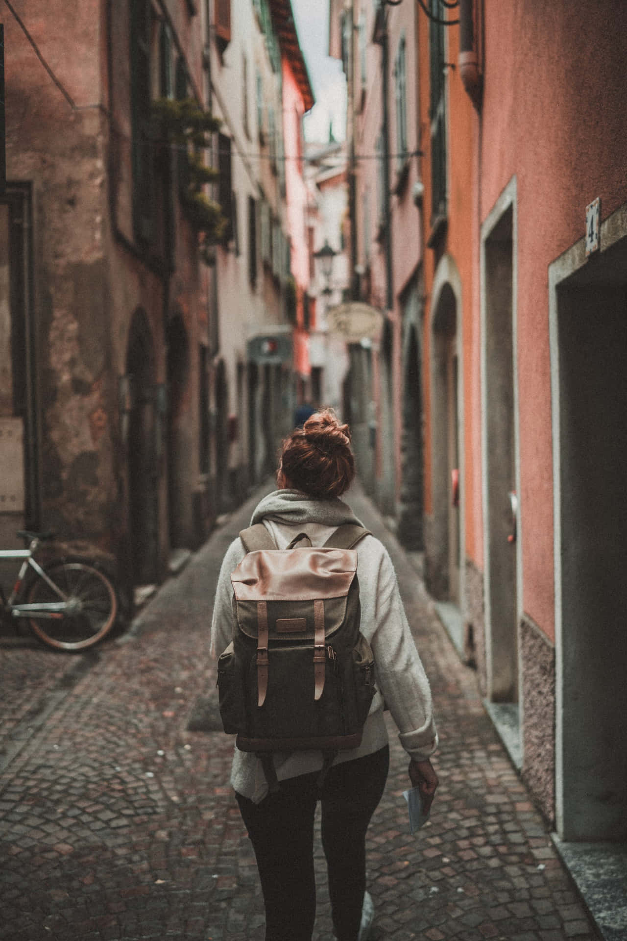 En kvinde går ned ad en smal gade med en rygsæk Wallpaper