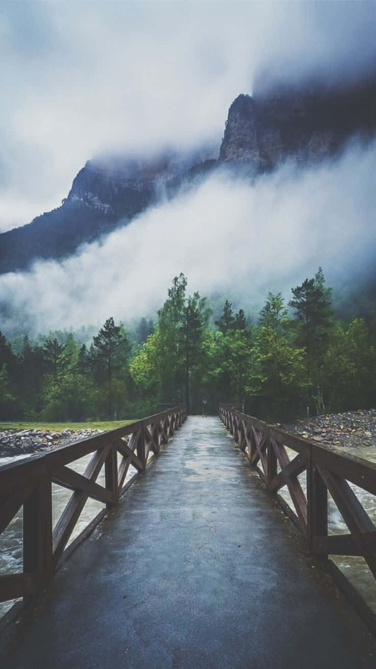 A Wooden Bridge Leading To A Mountain In The Fog Wallpaper