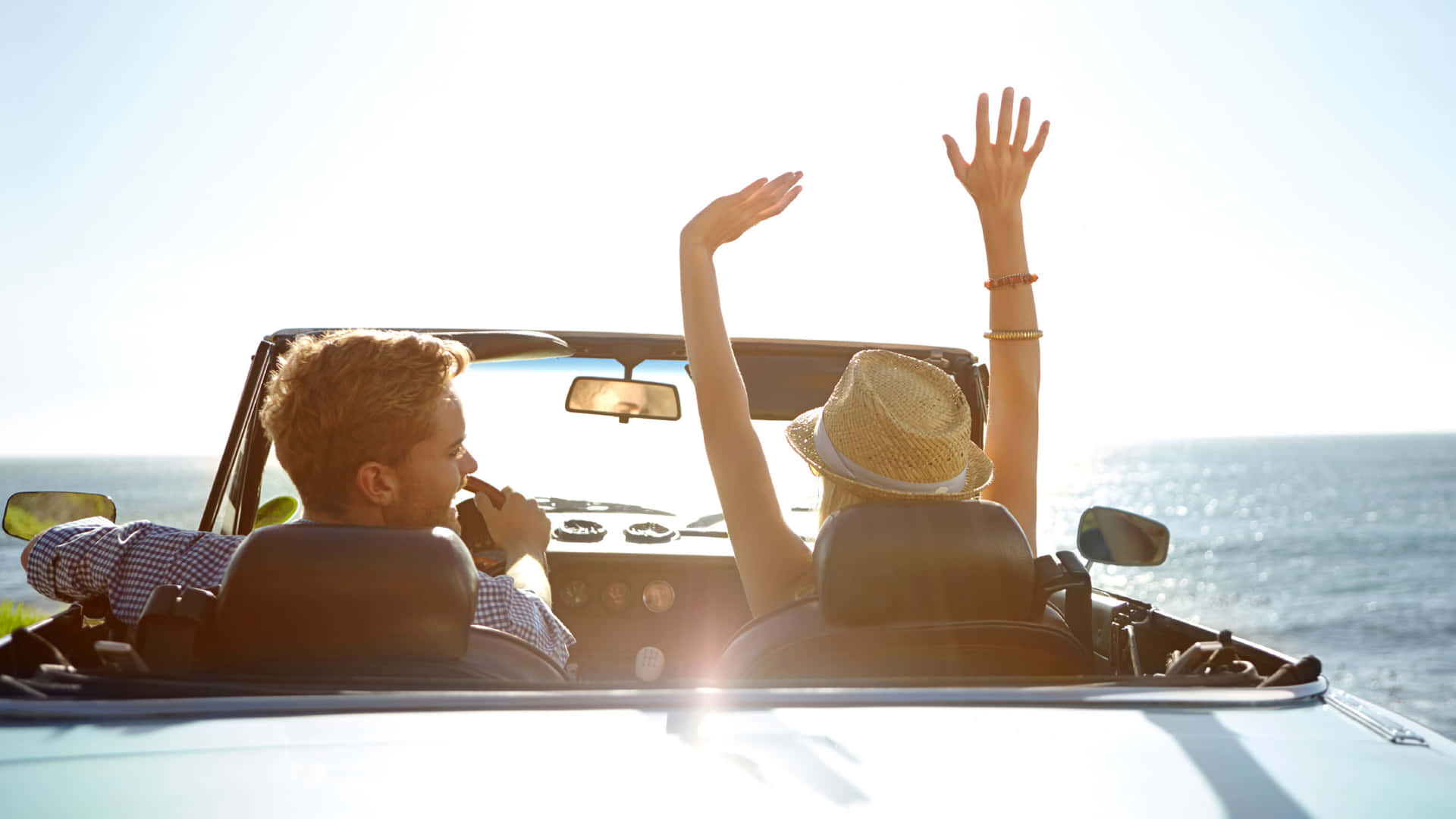 a couple in a convertible car with their hands raised