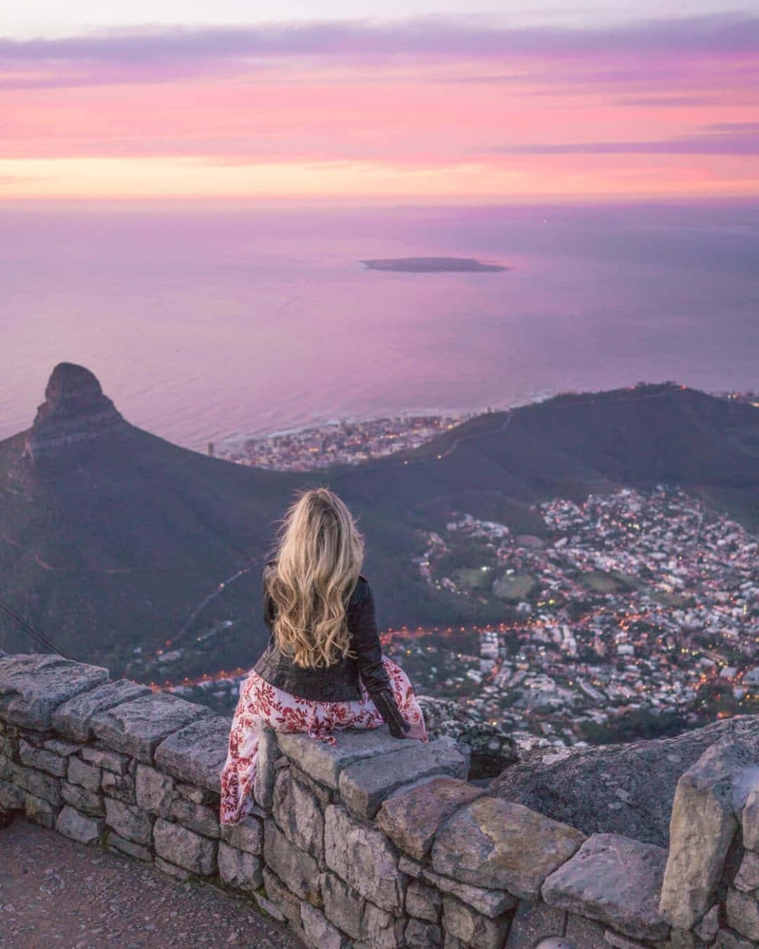 a woman is sitting on a rock overlooking the city of cape town
