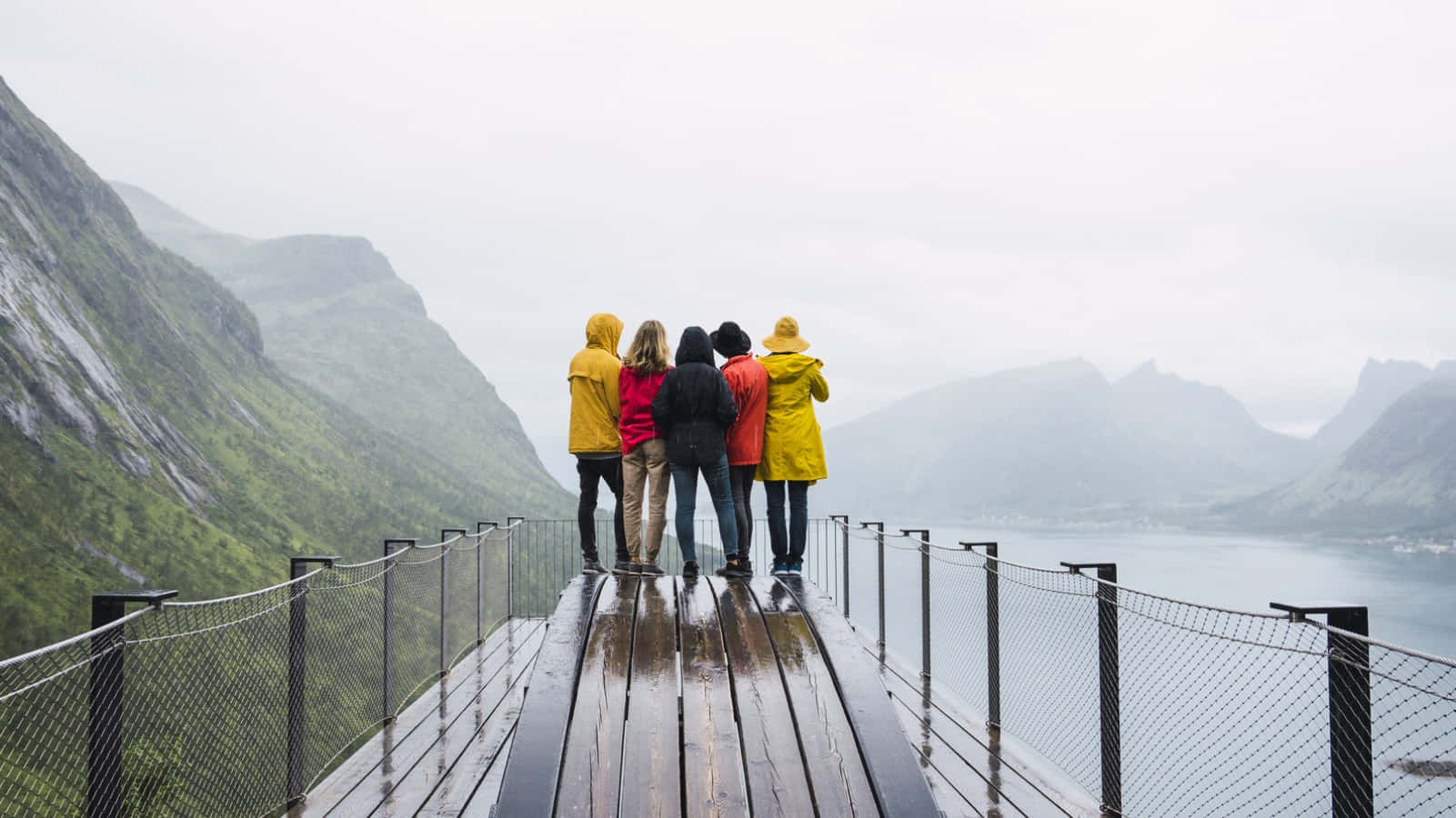 three people standing on a bridge looking at a lake