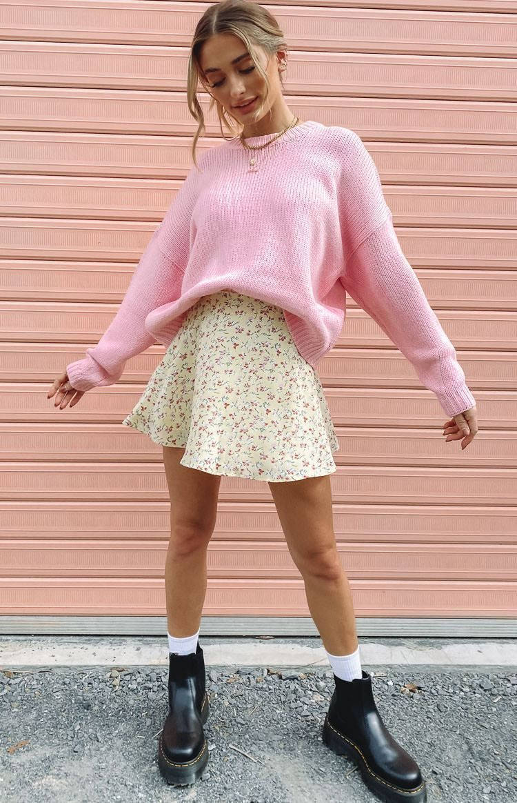 A Woman Wearing A Pink Sweater And A Floral Skirt Wallpaper