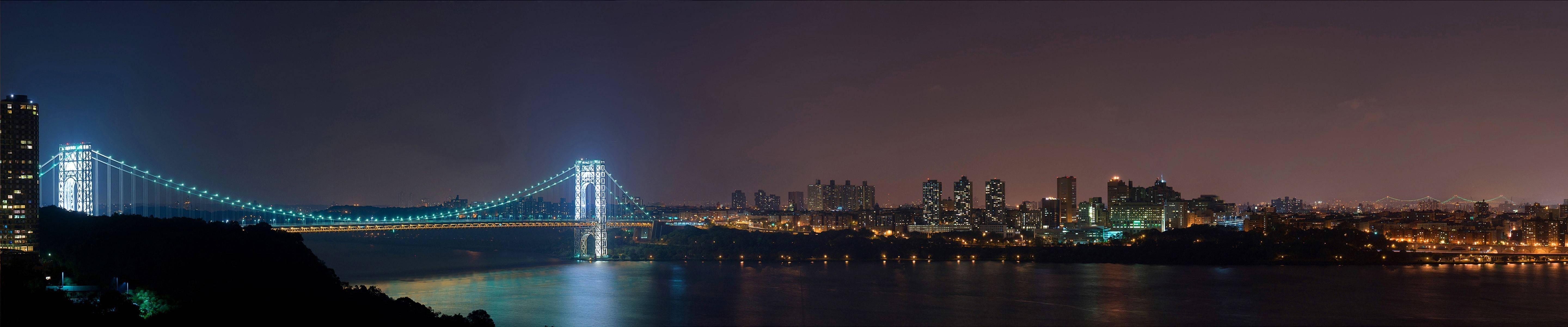Triple Monitor showing city lights, tall buildings from afar and a long lighted bridge.