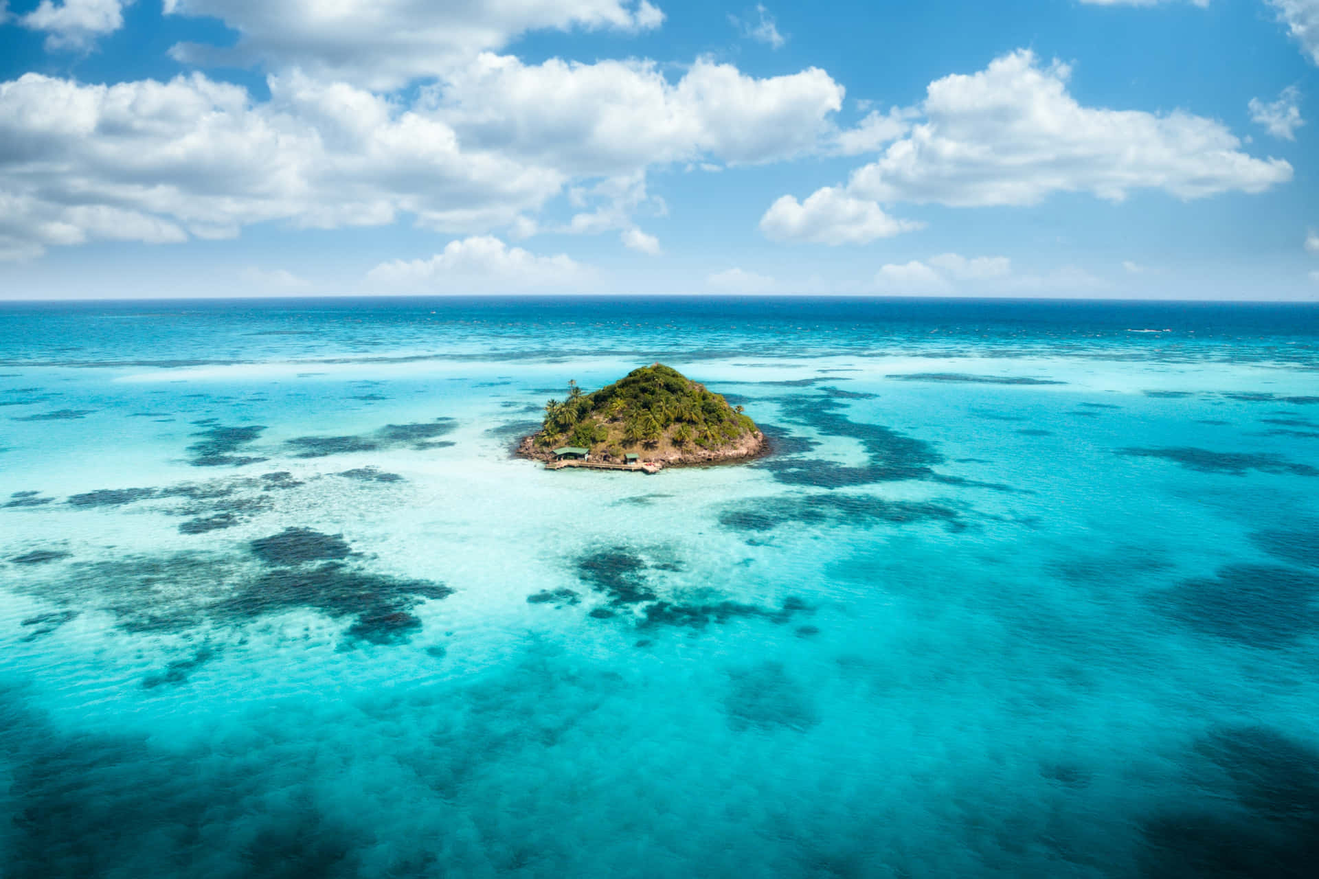 An Island In The Ocean With Blue Water And Clouds Wallpaper